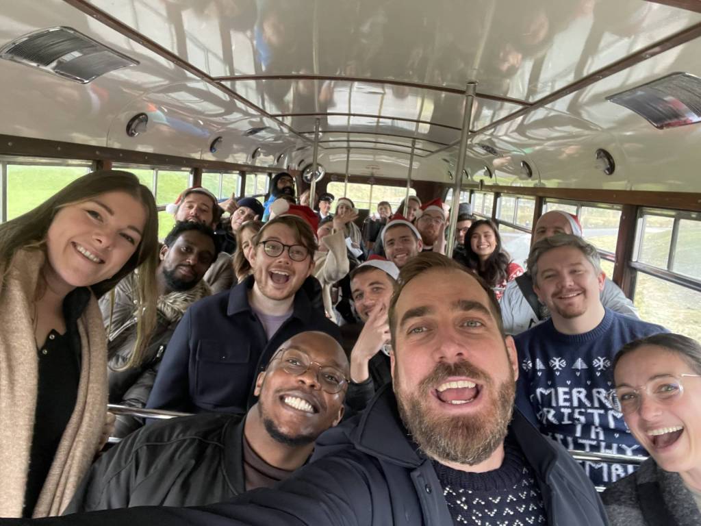 A big group of the Substrakt team on the top deck of a bus smiling. Someone at the front has taken a selfie so you can see everyone leaning in.