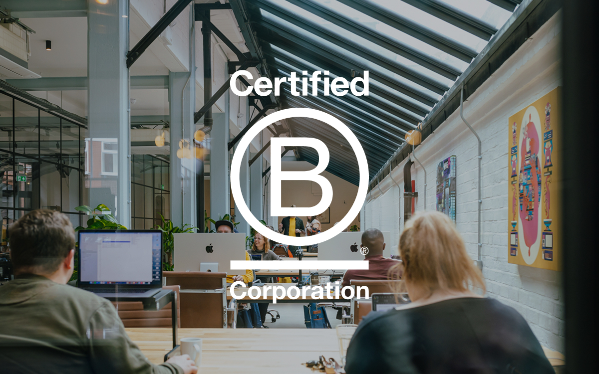 The B Corp logo overlaying an image of Substrakt's office. The office is big and airy, with colourful artwork on the walls. People are sat at their desks working.