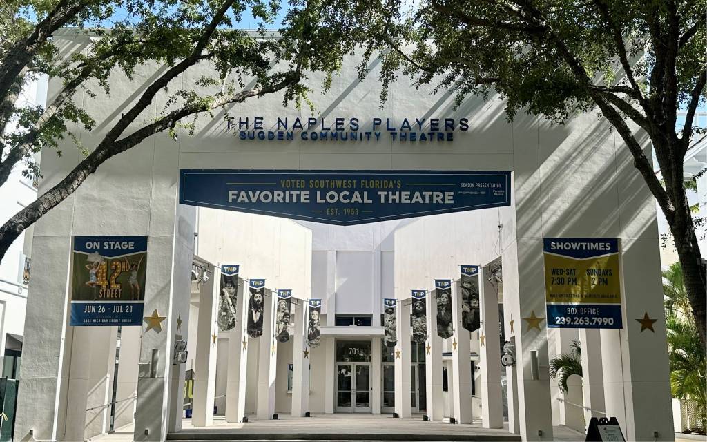 The external building of The Naples Players, white columns with banners hanging down.